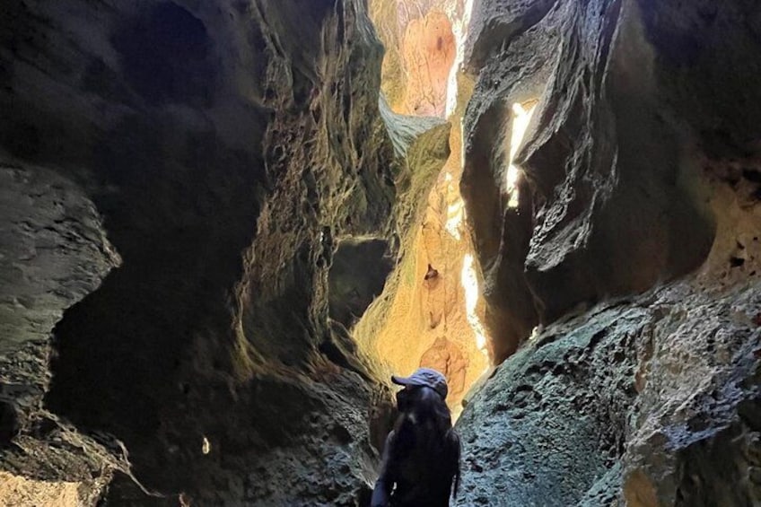 A person in a cave with a backpack, rocky walls, and a narrow passageway. 1