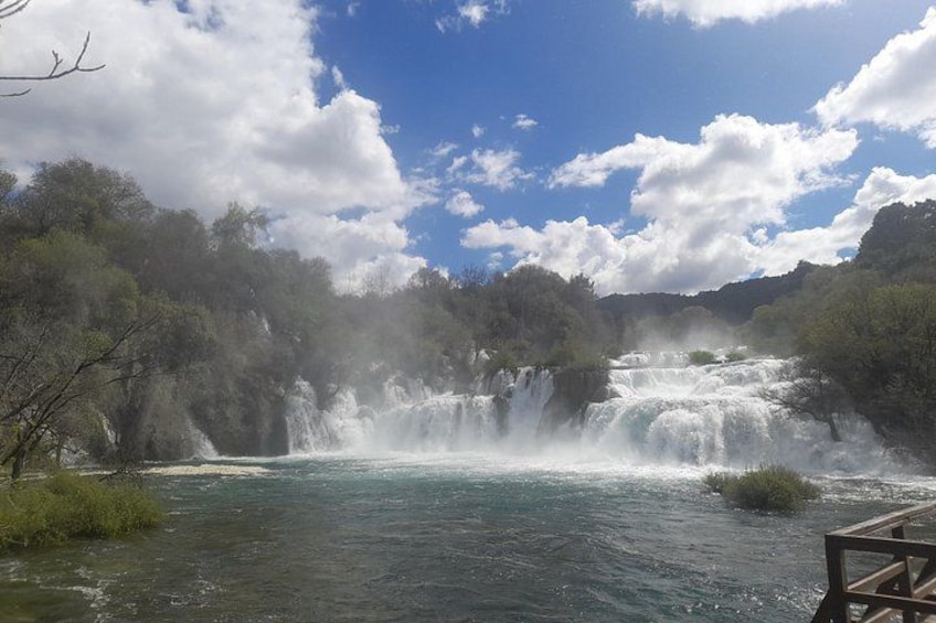 A waterfall cascading over rocks, surrounded by lush greenery and a clear blue sky. 3