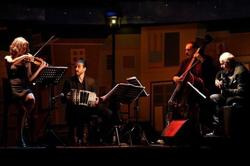 Un violinista, un acordeonista y un chelista interpretan en el escenario con atril para partituras. 2