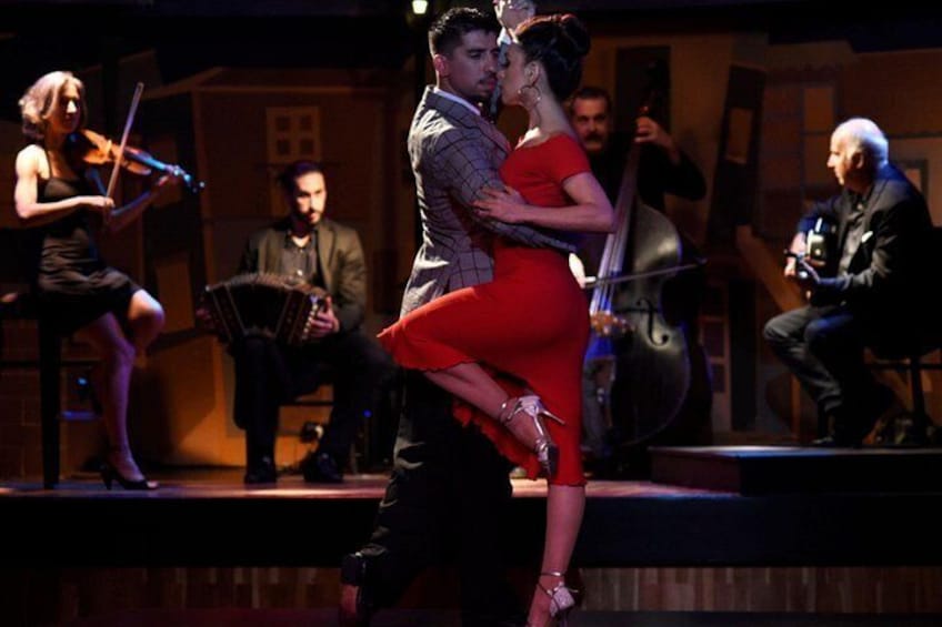 Una pareja bailando en un escenario, con un violinista y un cellista de fondo. 1