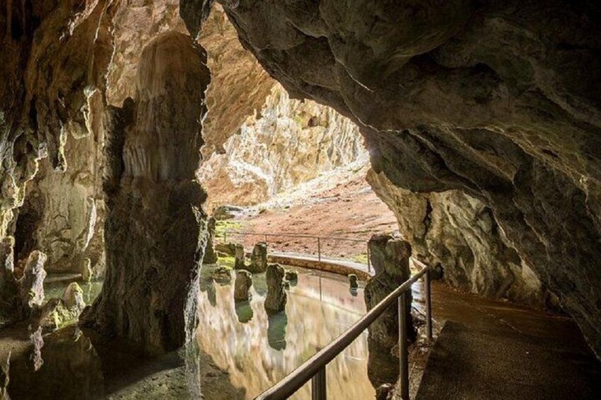 Una cueva con estalactitas, un pasillo de madera y un estanque de agua que refleja el entorno. 3