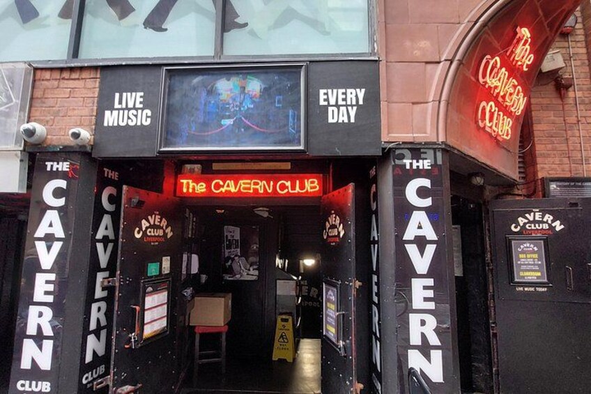 Entrada al Cavern Club con letreros de neón, una pantalla de televisión y una escalera. 5