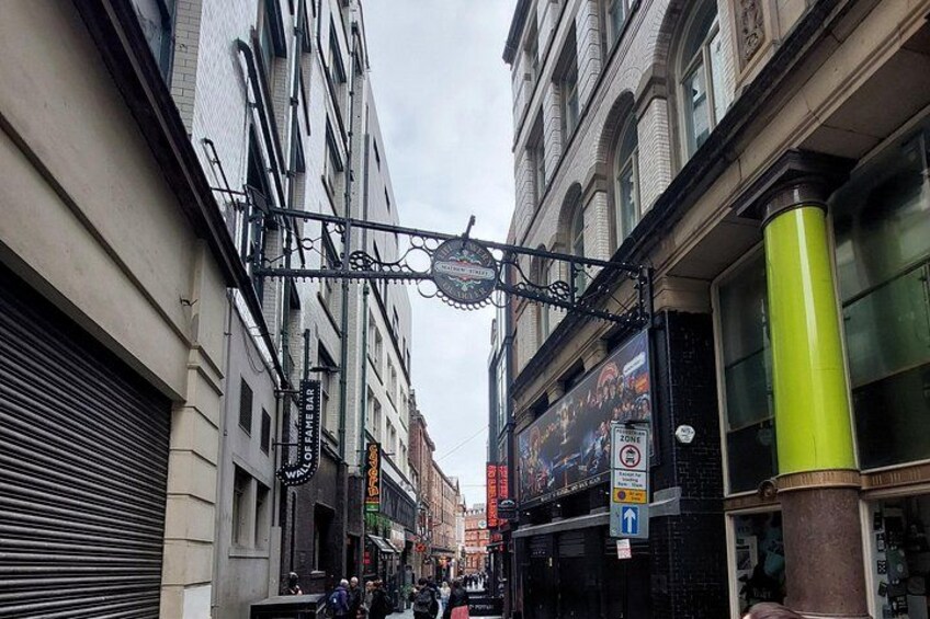 Una calle estrecha con un letrero de metal negro, un pilar verde y una tienda cerrada con una persiana. 3