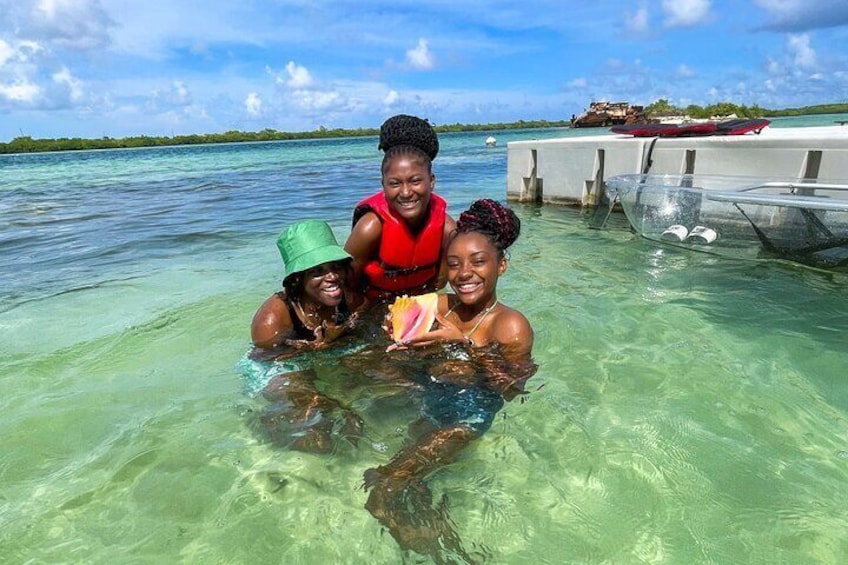 Tres personas en aguas tropicales cristalinas, un muelle y un bote al fondo. 1