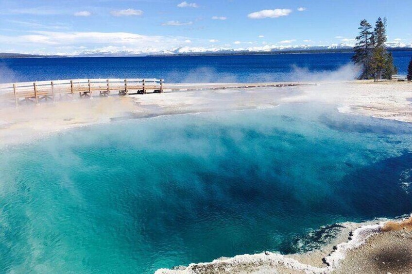A geothermal hot spring with clear turquoise water, a wooden viewing platform, and a snowy mountain in the background. 1