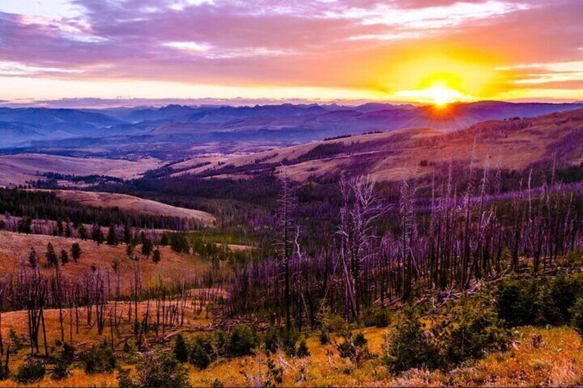 A sunset over a mountainous landscape with trees and hills. 2