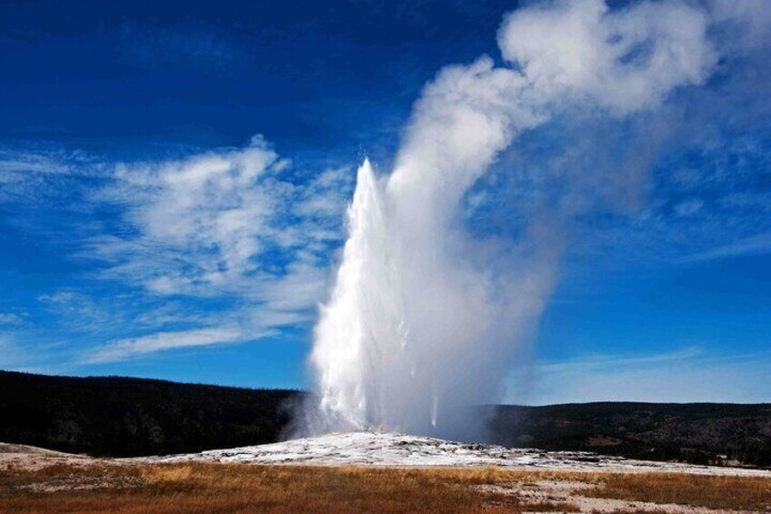 A geyser erupting with steam against a clear blue sky. 4