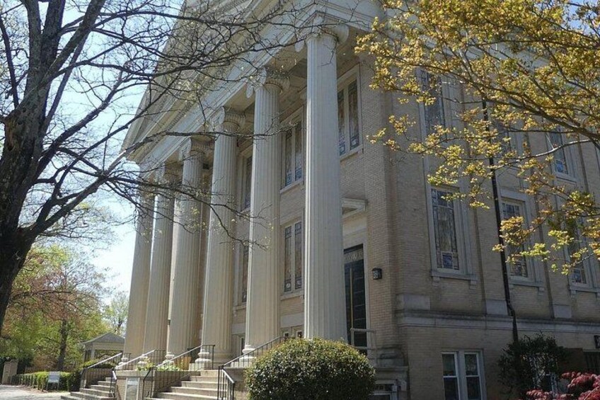 A large building with columns, a staircase, and a tree with yellow leaves. 1