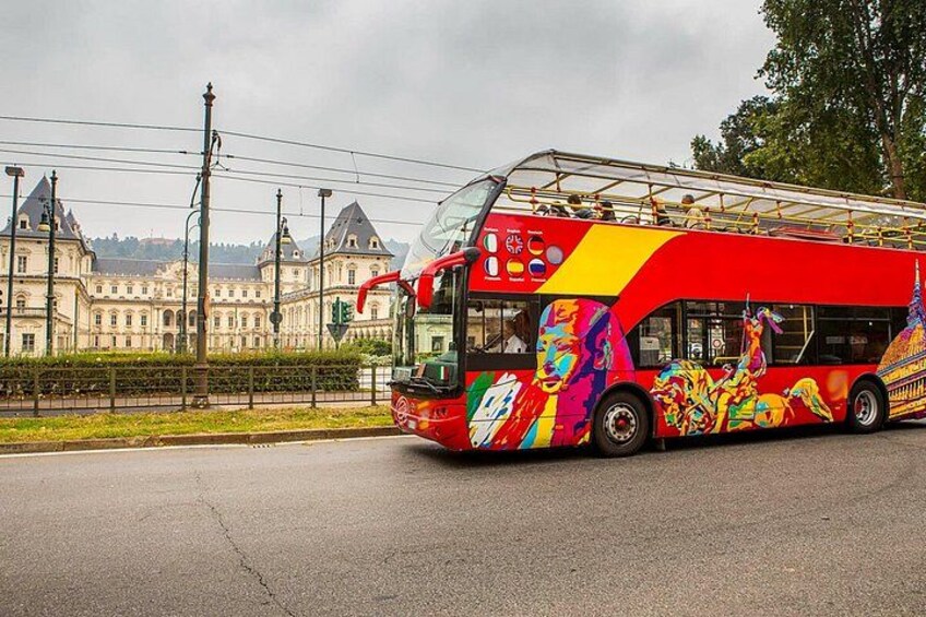 A colorful double-decker bus with a vibrant design, parked on a road with a historic building in the background. 5