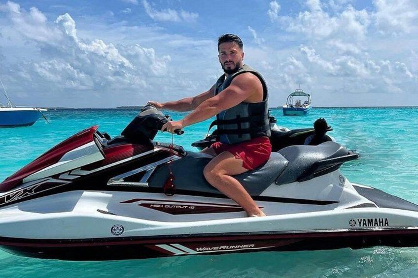 A person riding a Yamaha jet ski on turquoise water with boats in the background. 4