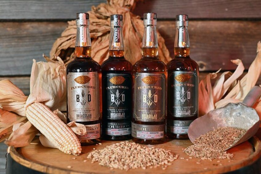 Four bottles of Blue Curried Vodka on a wooden surface with corn cobs and grains around them. 1