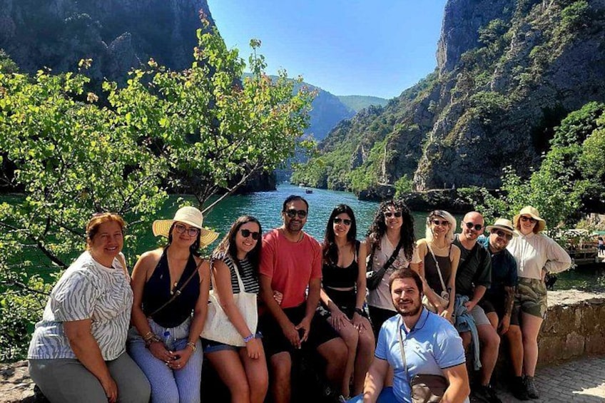 Un groupe de personnes posant dans un cadre naturel, avec une rivière et des falaises en arrière-plan. 1