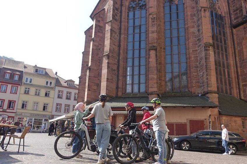A group of people with bicycles in front of a large brick building with large windows. 3
