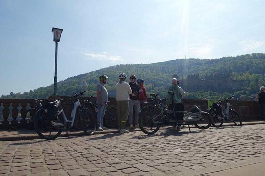 A group of people standing on a bridge with bicycles, overlooking a hilly landscape. 5