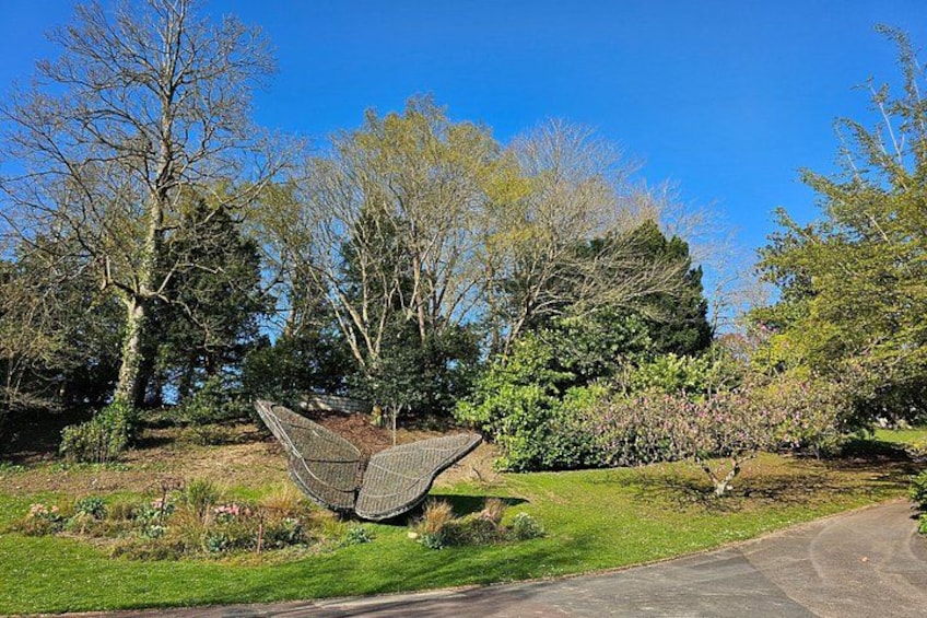 A garden with a large metal sculpture, trees, and a paved path. 3