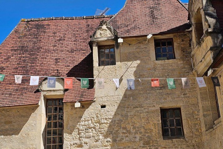 A historic building with a red-tiled roof, stone walls, and a series of flags. 4
