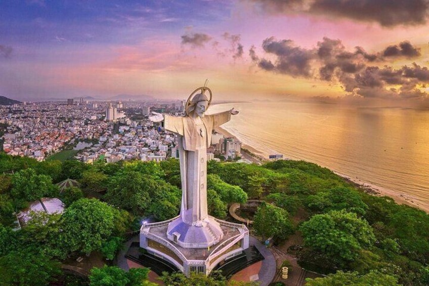 A large statue of a figure with outstretched arms, surrounded by lush greenery and overlooking a coastal cityscape. 1