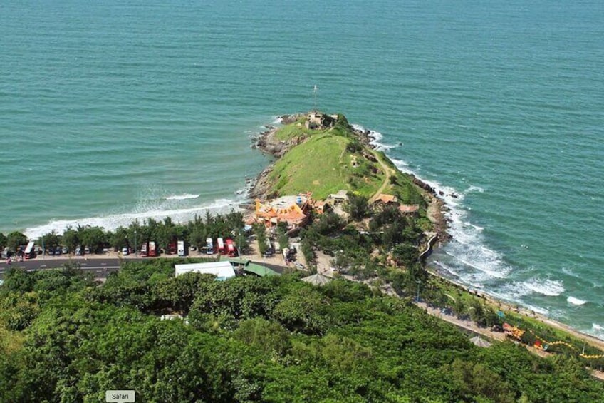 An aerial view of a coastal area with a grassy hill, a lighthouse, and a road leading to a beach. 5