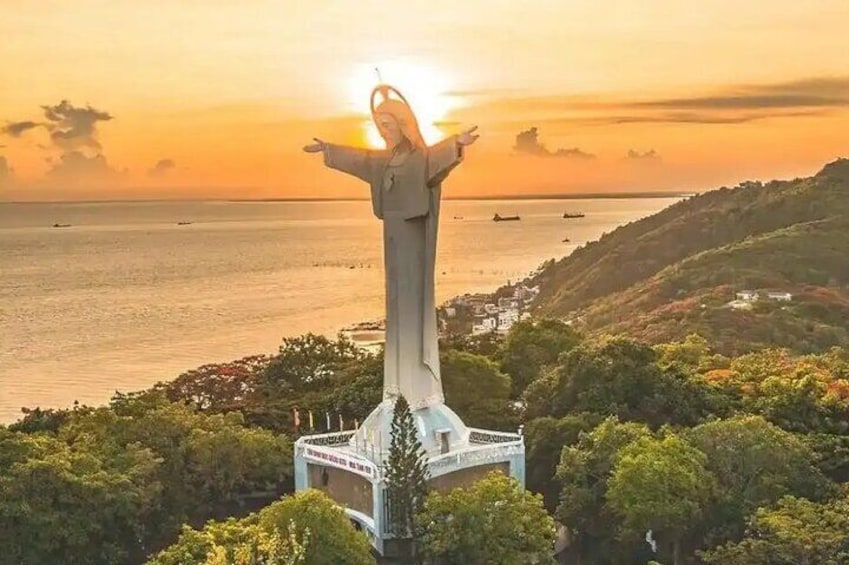 A statue with outstretched arms overlooking a coastal landscape during sunset. 2
