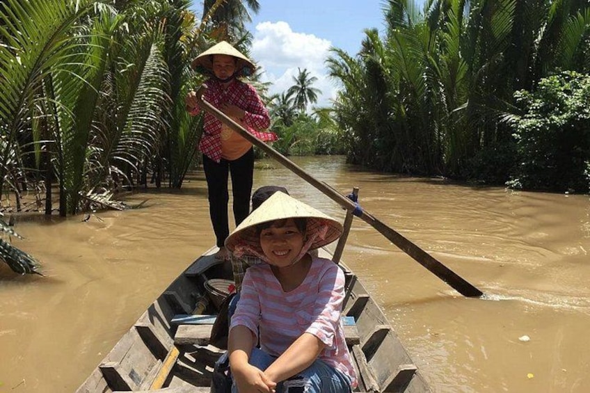 Two people in a boat on a river, surrounded by palm trees. 2