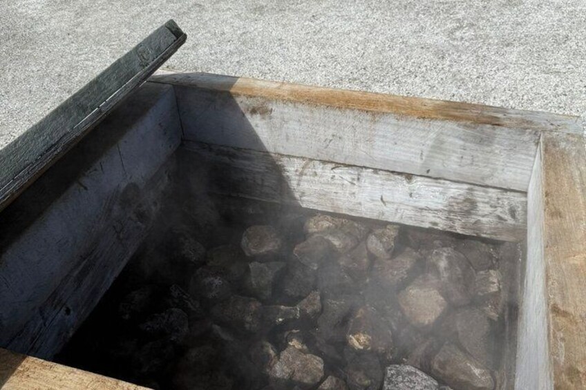 A metal container with a wooden lid, filled with rocks and emitting steam. 3