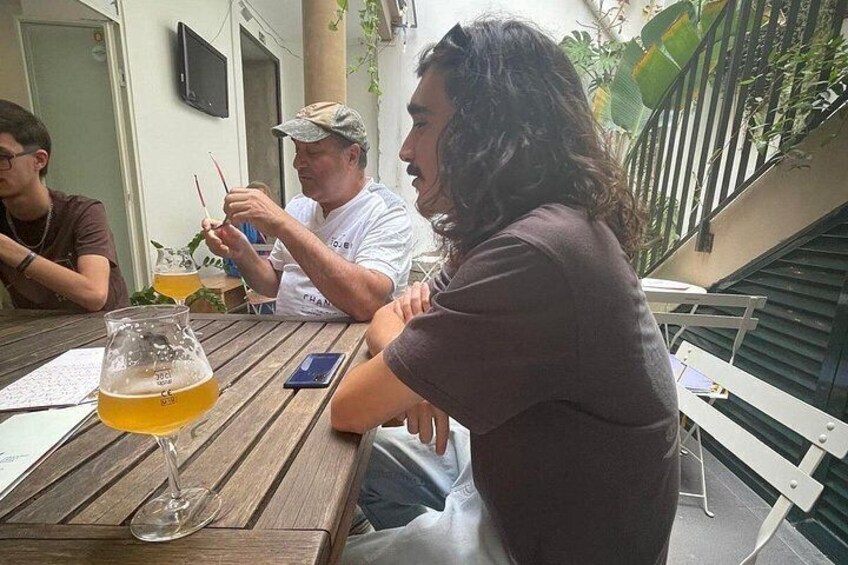 A group of people sitting at a wooden table outdoors, with drinks and a smartphone on the table. 2