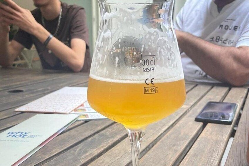 A glass of beer on a wooden table with a person in the background. 3