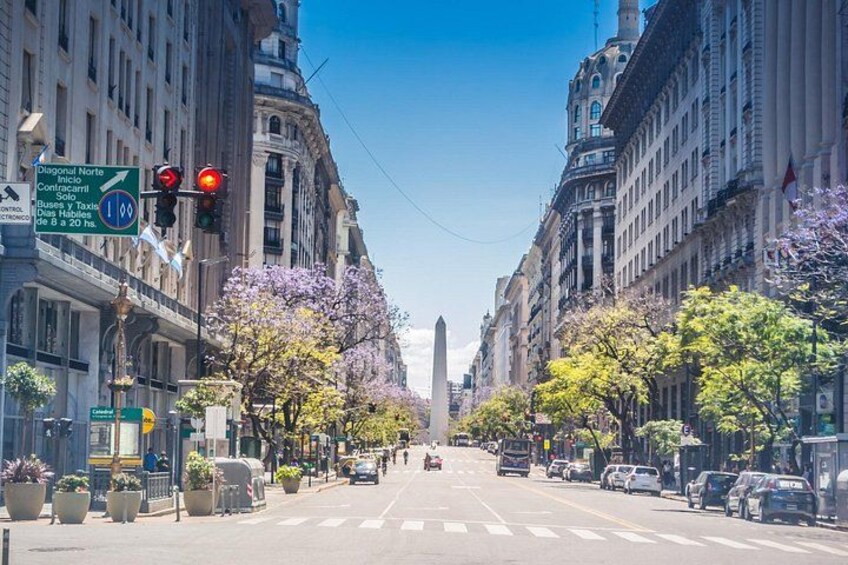 A city street lined with historic buildings, a traffic light, and a clear blue sky. 2