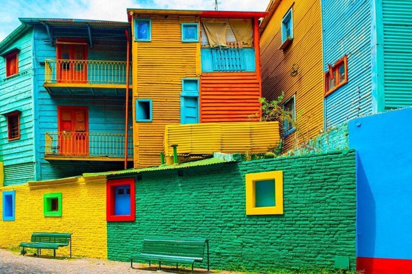 Colorful buildings with balconies, a green wall, and a bench. 4