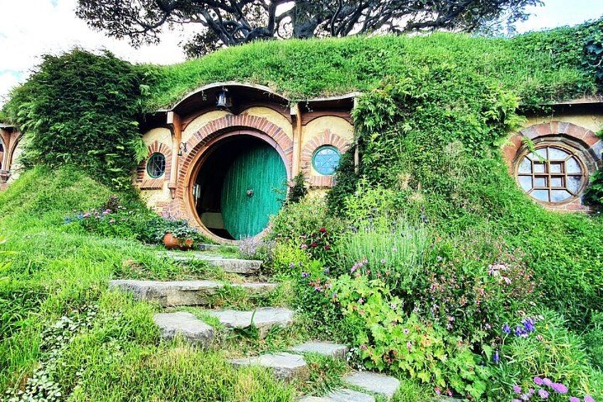 Hobbit-style houses with round doors and green shutters, surrounded by lush greenery and stone steps. 3