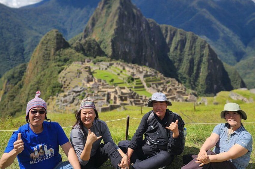 Un gruppo di persone seduto di fronte a Machu Picchu, con un paesaggio montuoso sullo sfondo. 1