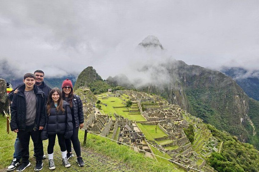 Un gruppo di persone in piedi su una sporgenza erbosa con vista su Machu Picchu, avvolto dalla nebbia. 4