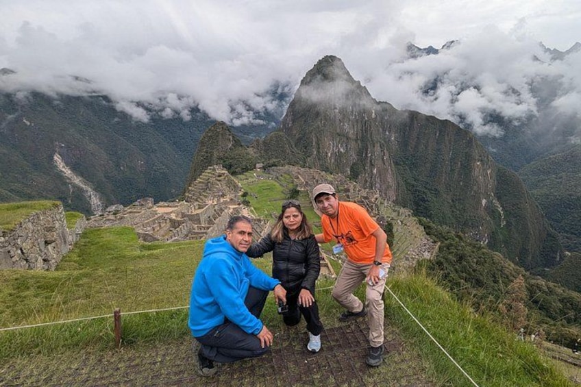 Tre persone in posa di fronte alle rovine di Machu Picchu, con un paesaggio montuoso sullo sfondo. 2