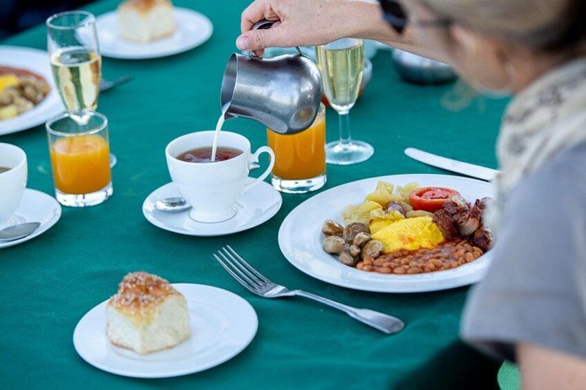 Ein Frühstückstisch mit grüner Tischdecke, einer Kaffeetasse, Orangensaft, einem Teller mit Eiern, Bohnen und einem Stück Kuchen. 2