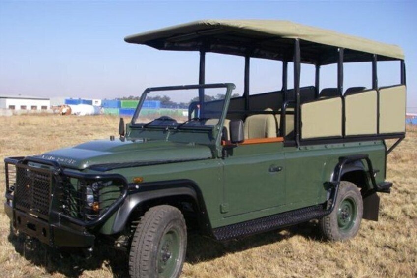 A green Land Rover with a roof rack parked on a field. 2
