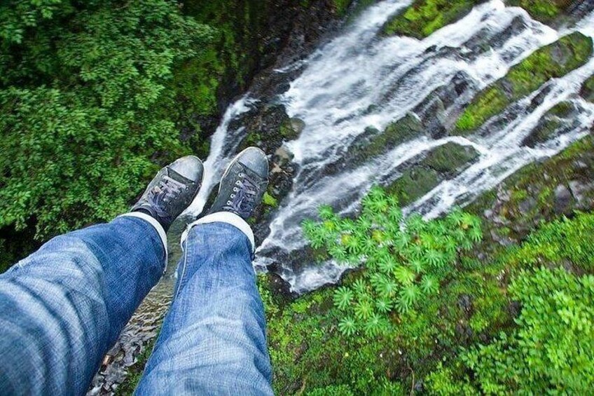 A person sitting with legs crossed, overlooking a waterfall surrounded by lush greenery. 4