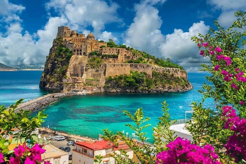 A coastal fortress on a cliff, turquoise waters, and pink flowers. 1