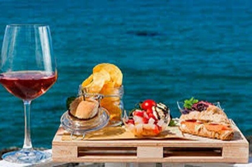 A wooden board with food items and a glass of red wine against a blue background. 2
