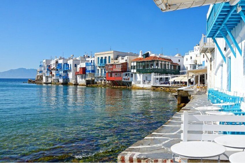 A coastal town with colorful buildings, a clear blue sea, and outdoor seating by the water. 5