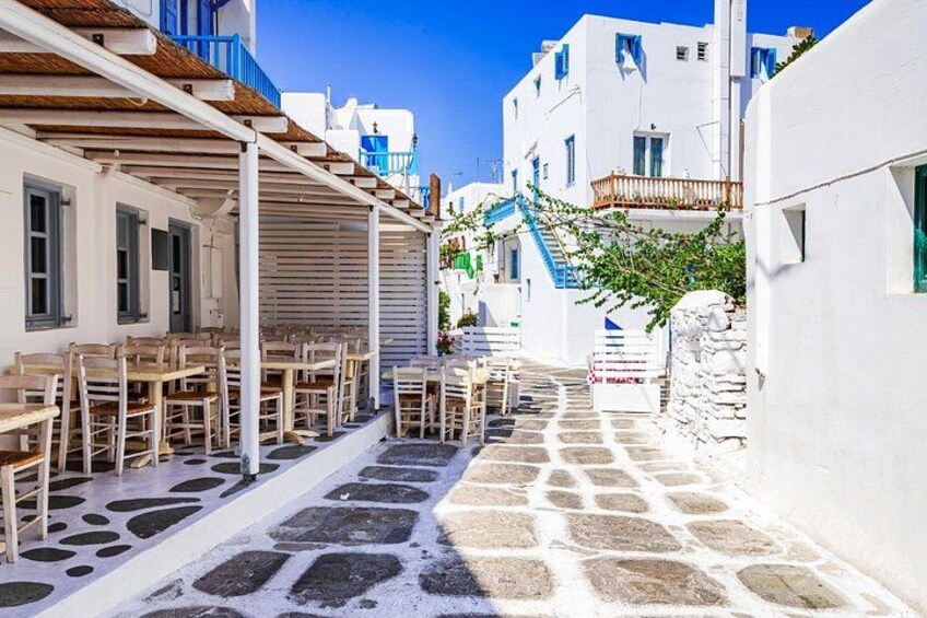 A narrow street with white buildings, blue accents, and outdoor seating. 4