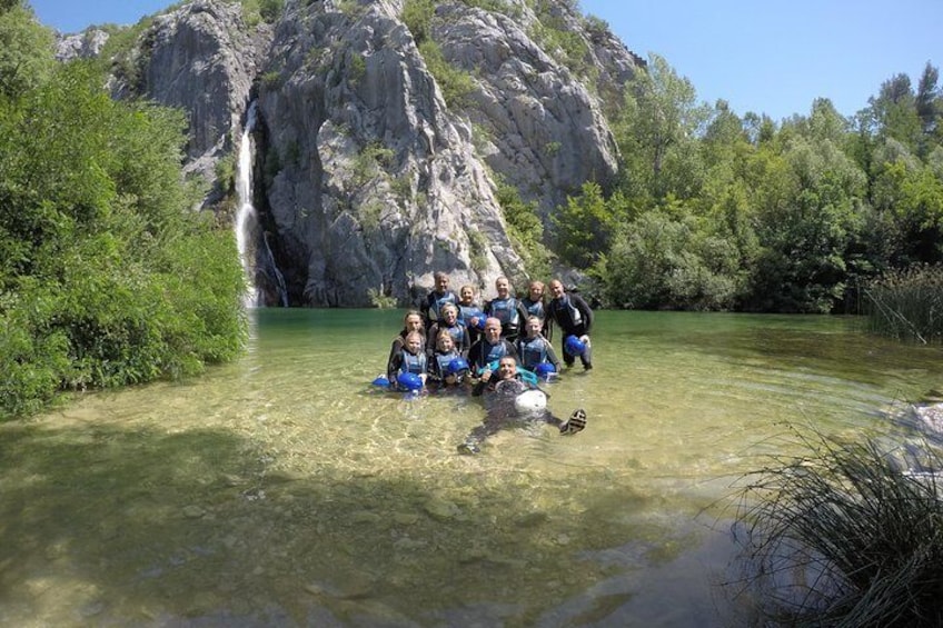 Un groupe de personnes posant dans une rivière peu profonde, entourée de falaises rocheuses et de verdure. 1