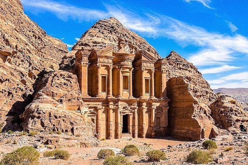 A rock-cut temple with columns and a facade, surrounded by rugged mountains. 1