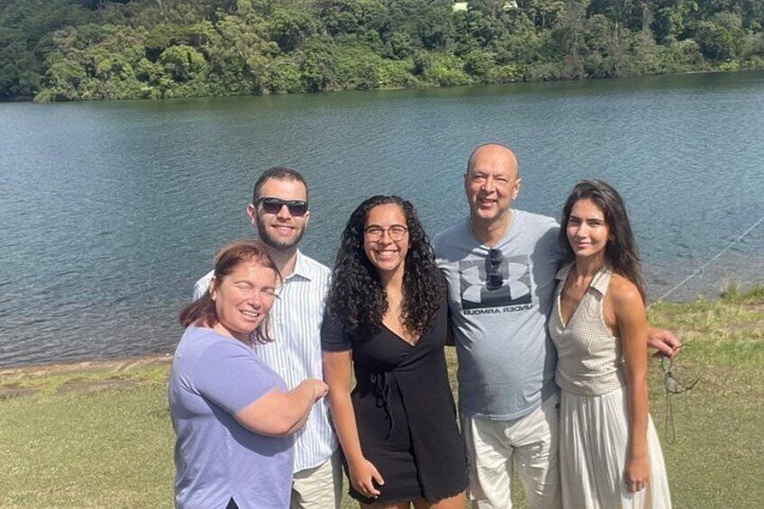 A group of people standing by a lake with a forested background. 2