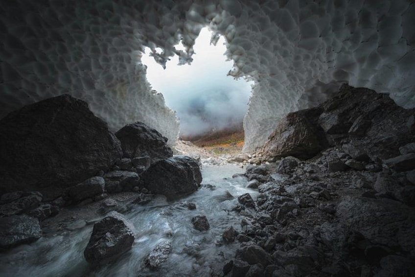 An ice cave with a rocky interior and a view of a cloudy landscape. 1