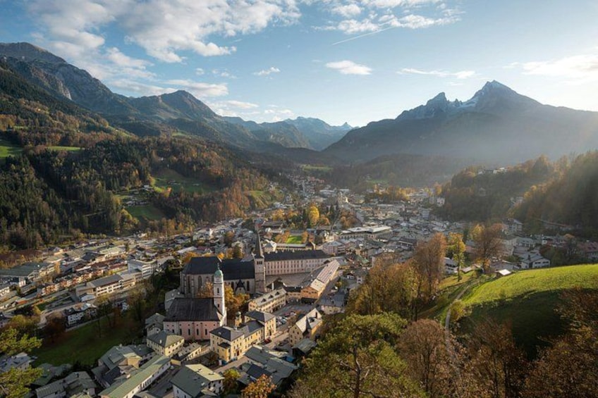 A town nestled in a valley with mountains in the background, surrounded by greenery and featuring prominent buildings including a church with a tall steeple. 2