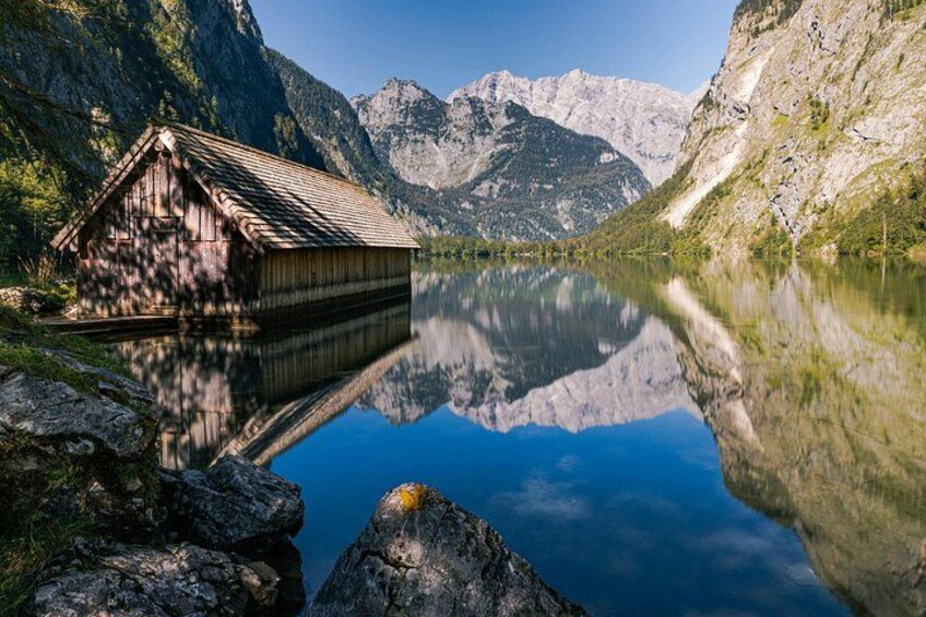 A wooden cabin by a calm lake with mountains in the background. 5