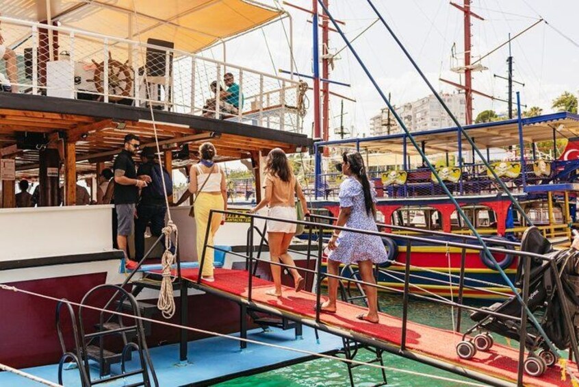 Eine Gruppe von Menschen auf einem Bootsdeck mit einer Strickleiter und einem farbenfrohen Boot im Hintergrund. 5