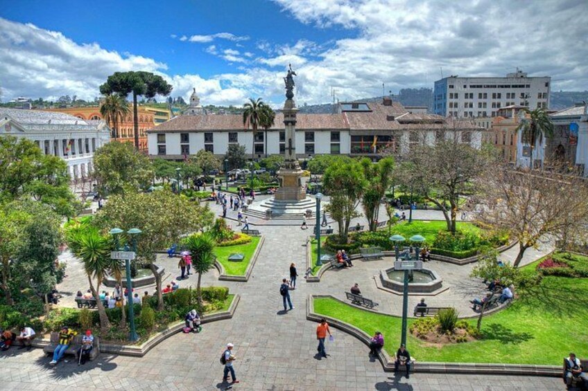 Una plaza con un monumento central, rodeada de zonas verdes y edificios. 4