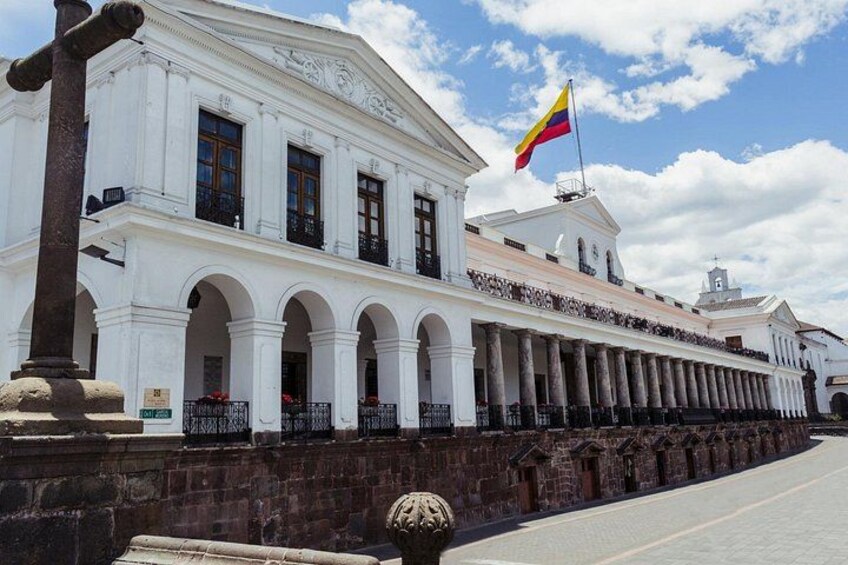 Un edificio de estilo colonial blanco con una bandera, columnas y una calle empedrada. 5