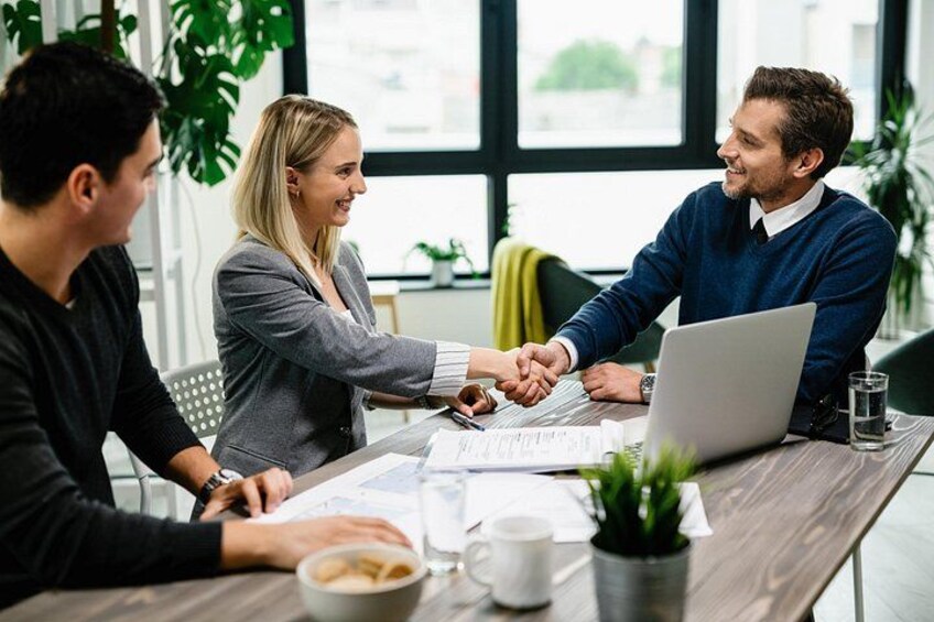 Three people shaking hands over a table with documents and a laptop. 2